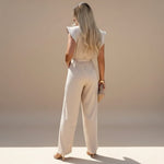Yemelia beige wide leg jumpsuit with flutter sleeves and adjustable waist tie. Elegant, full-length silhouette.